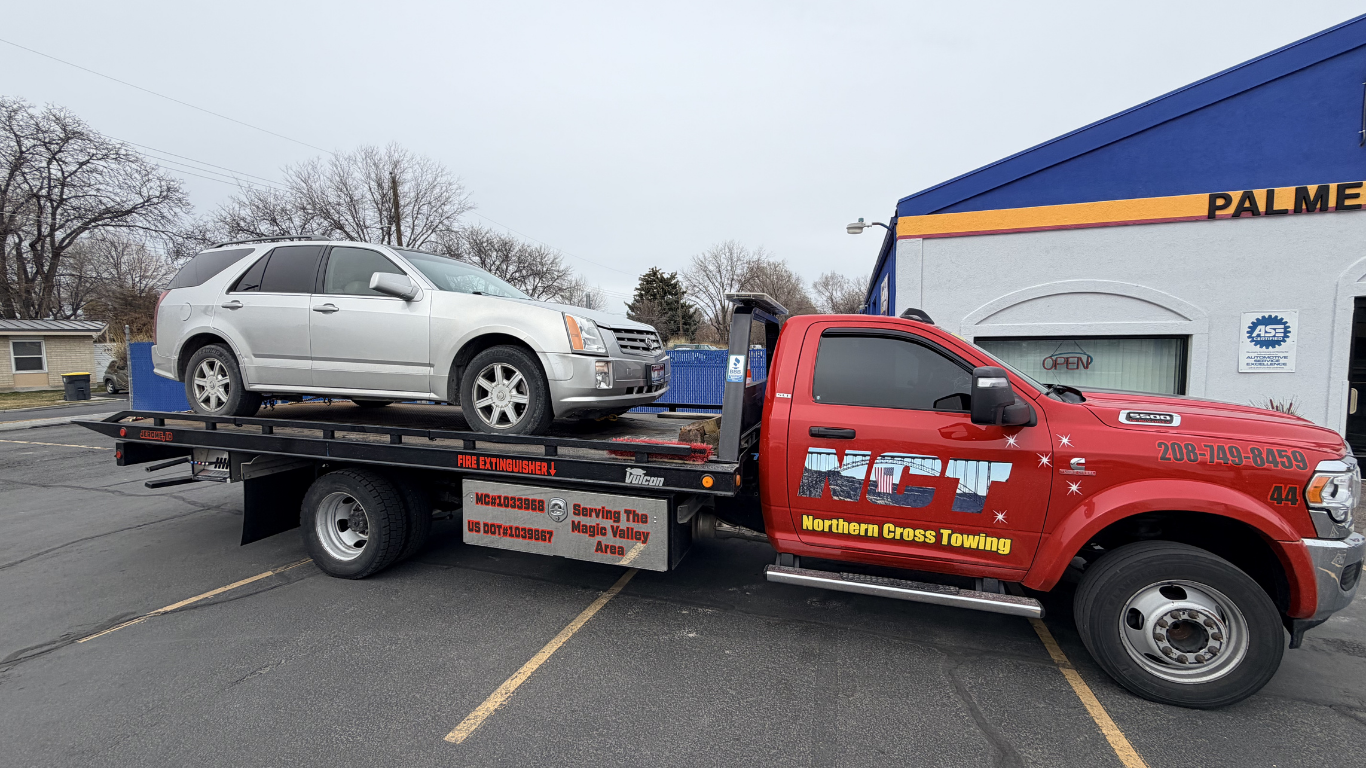 A silver SUV loaded on the back of a red flatbed tow truck parked in front of an automotive building.