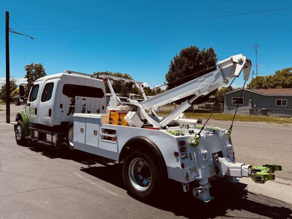 White tow truck with boom and wheel lift parked on a sunny street under a blue sky.