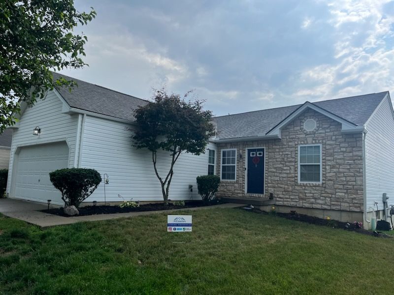 A white house with a gray roof and a sign in front of it.
