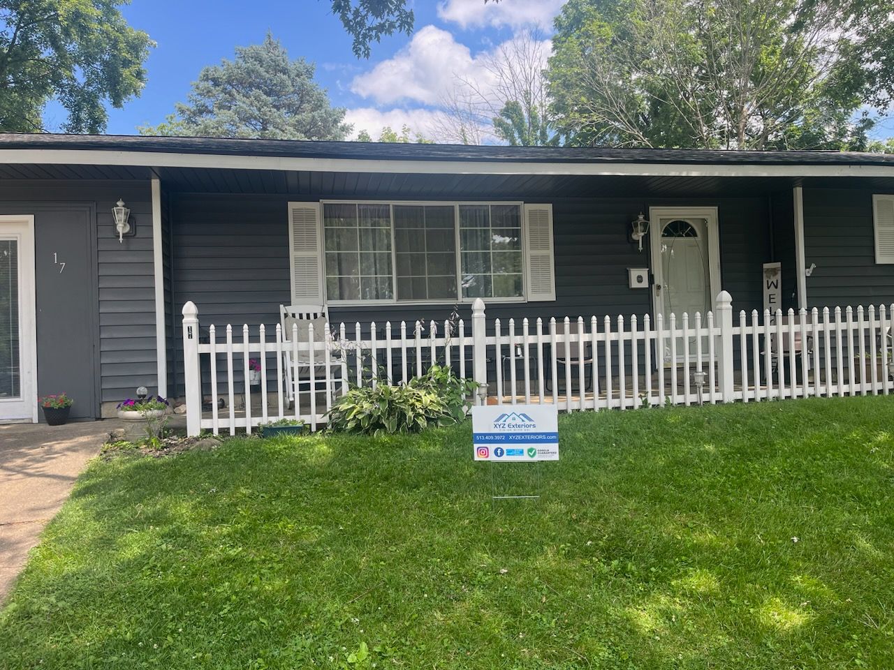 A black house with a white picket fence and a sign in front of it.