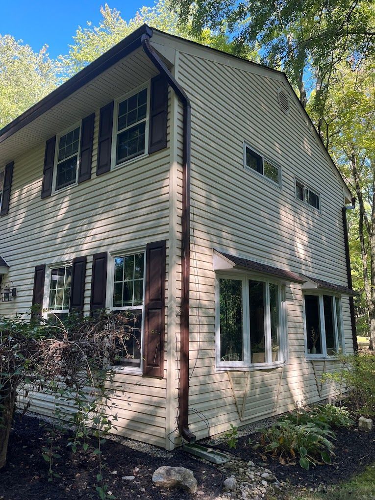 A white house with brown shutters and a gutter on the side of it.
