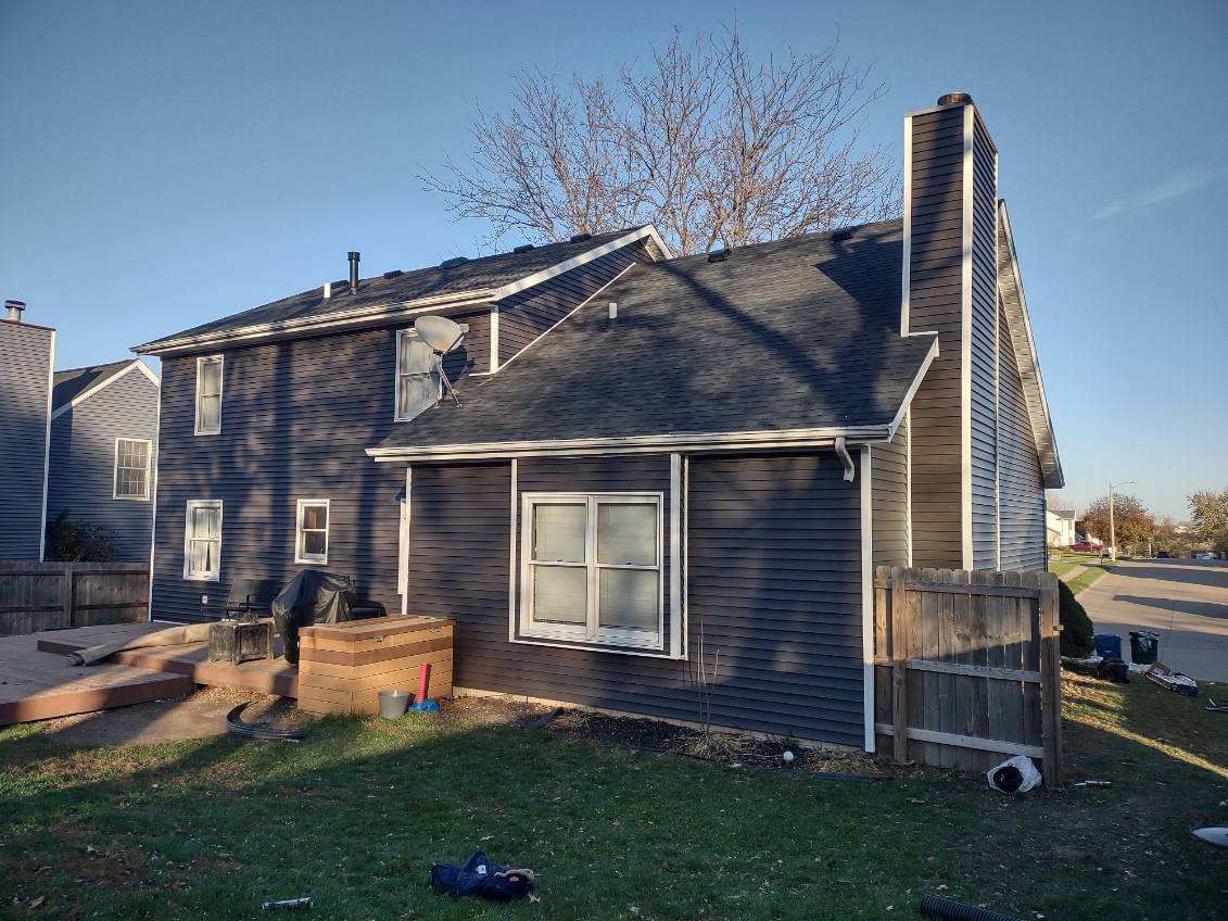 The back of a house with a black siding and a chimney.