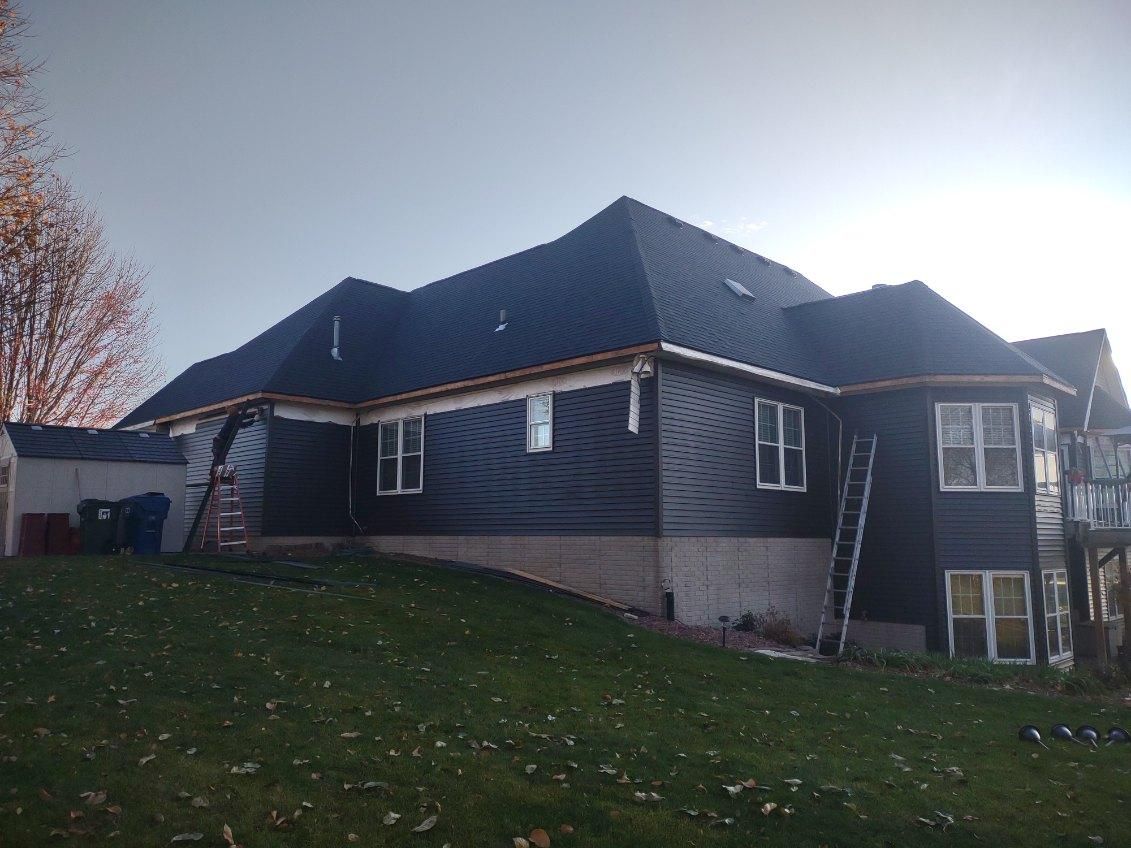 A large house with a black roof is sitting on top of a lush green hill.