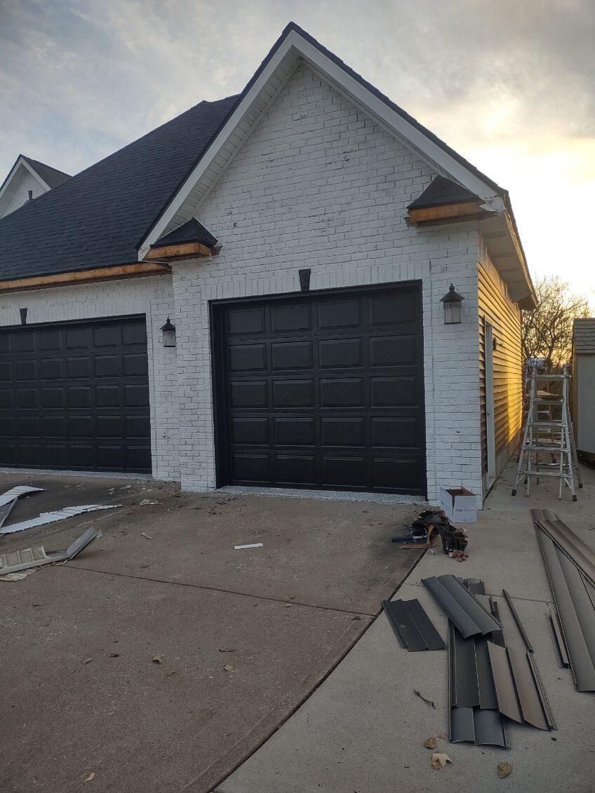 A white house with black garage doors is being built.