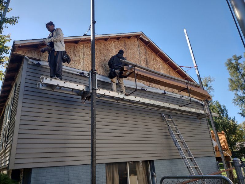 Two men are standing on a ladder on the side of a house.