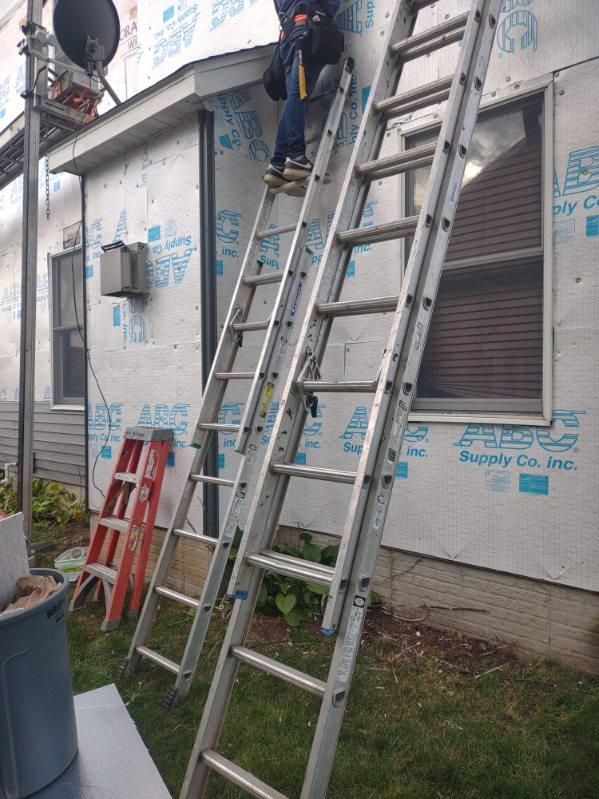 A man is standing on a ladder on the side of a house.