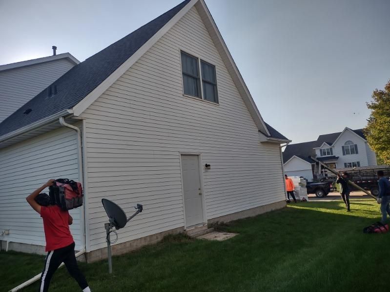 A man in a red shirt is standing in front of a white house.