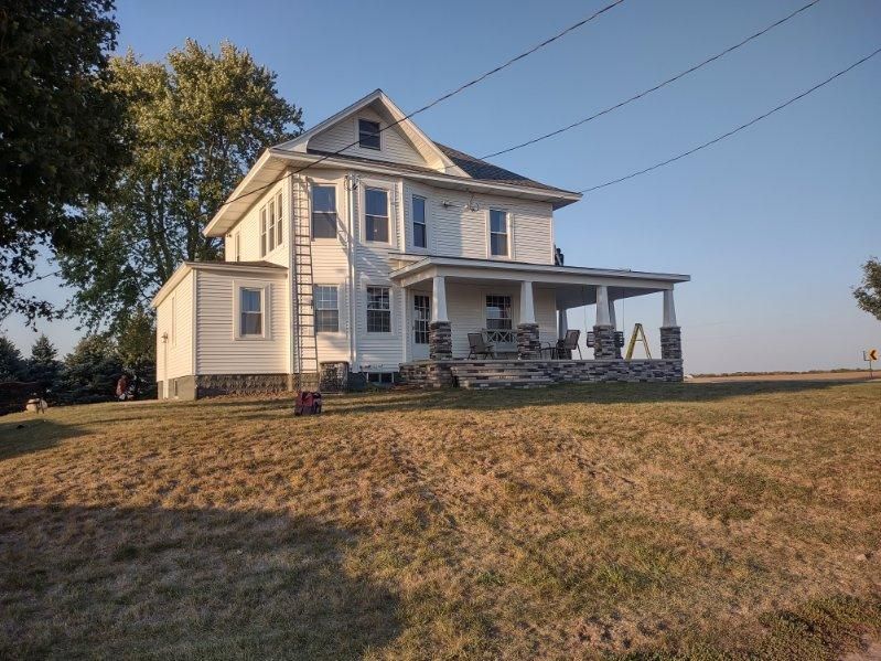 A large white house is sitting in the middle of a grassy field.