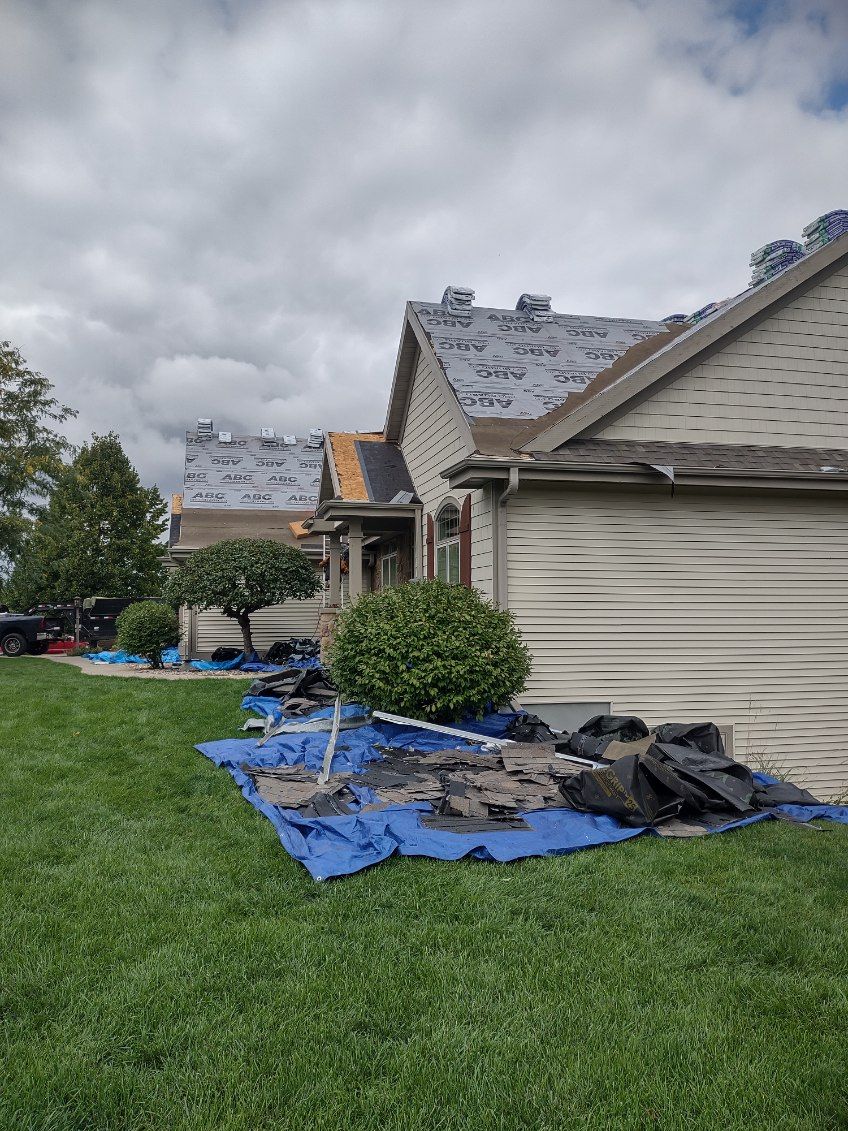 A house with a roof being installed is sitting on top of a lush green lawn.