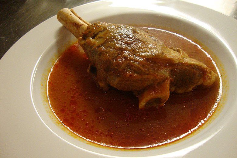 A white plate topped with a piece of meat in a sauce