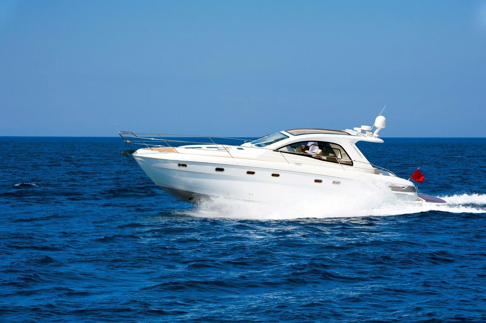 A white motor yacht cruising rapidly across deep blue, open ocean waters under a clear sky.