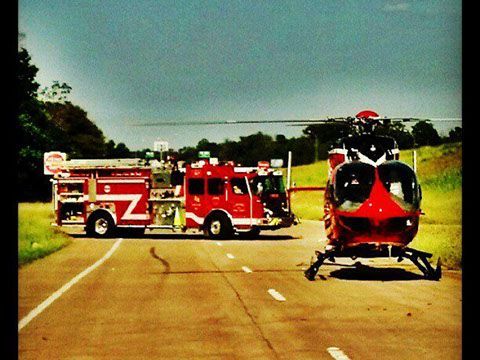 A red fire truck parked on a highway behind a life flight helicopter.