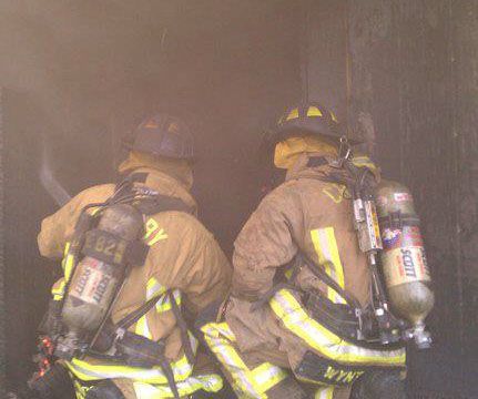 Two firefighters are standing next to each other in a spraying water on a fire during a training exercise
