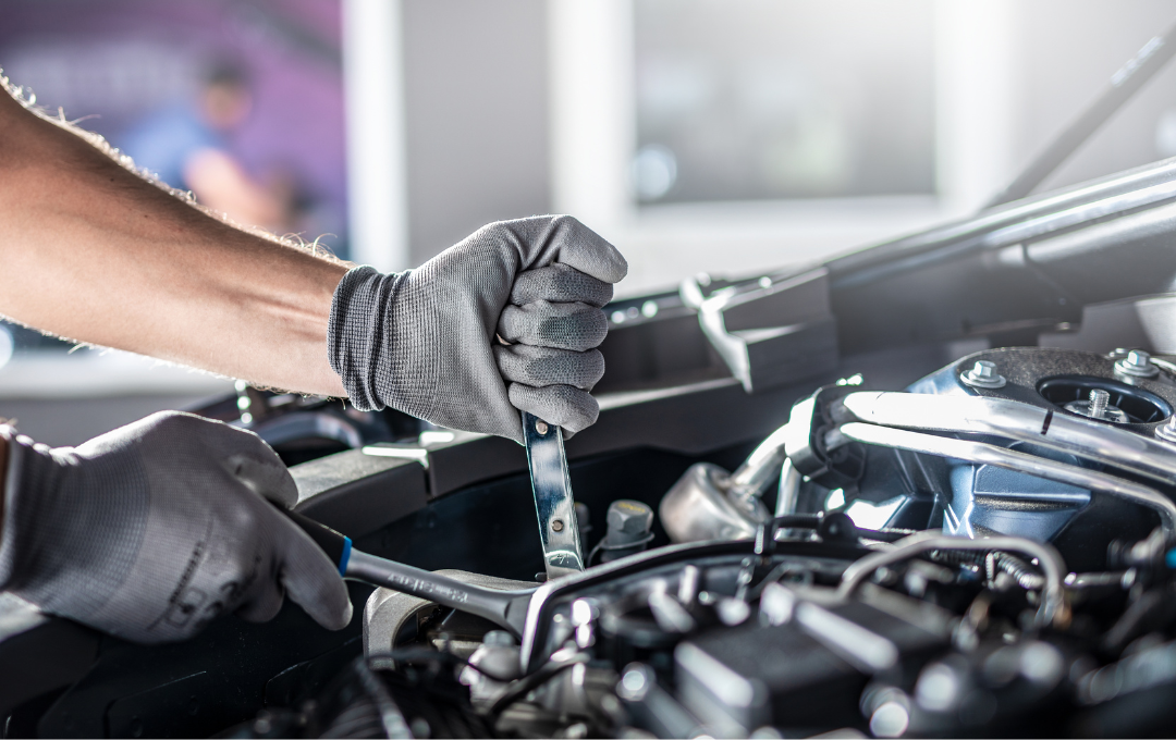 Mechanic in gloves using wrench on car engine in a garage.
