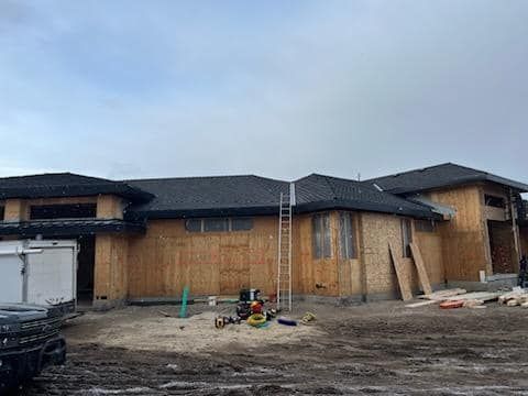 A large house is being built in the middle of a dirt field.