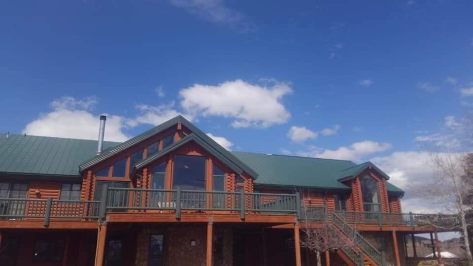 A large log cabin with a green roof and a large deck.