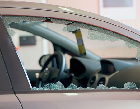 A side view of a car with a shattered driver-side window, showing glass fragments along the bottom of the frame.