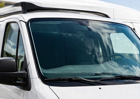 A close-up view of the front windshield and roof rack of a white van parked outdoors under a bright, sunny sky.