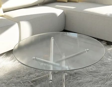 A round, glass-topped coffee table with a metal tripod base, positioned on a shaggy rug in front of a white sofa.
