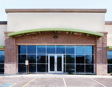Exterior of a commercial storefront with a beige facade, tan brick pillars, a green arched awning, and glass doors.