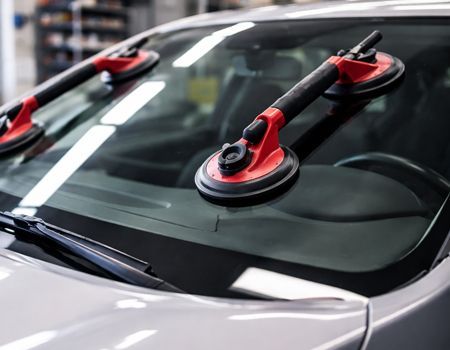 Two red and black suction cup handles attached to a car windshield for repair or removal.