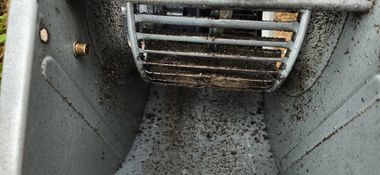 Dirty metal vent or grate with debris and stains inside a gray machine housing