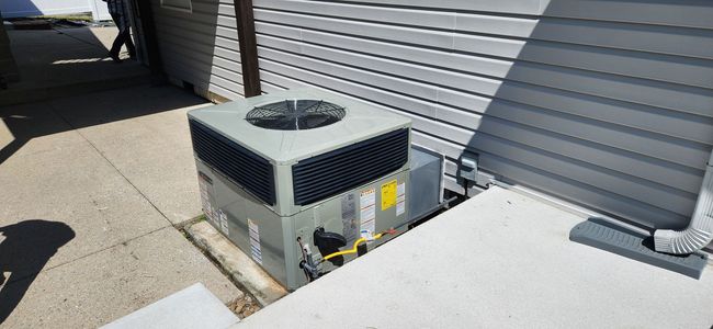 Outdoor HVAC unit beside a building wall on a sunny concrete rooftop or patio area