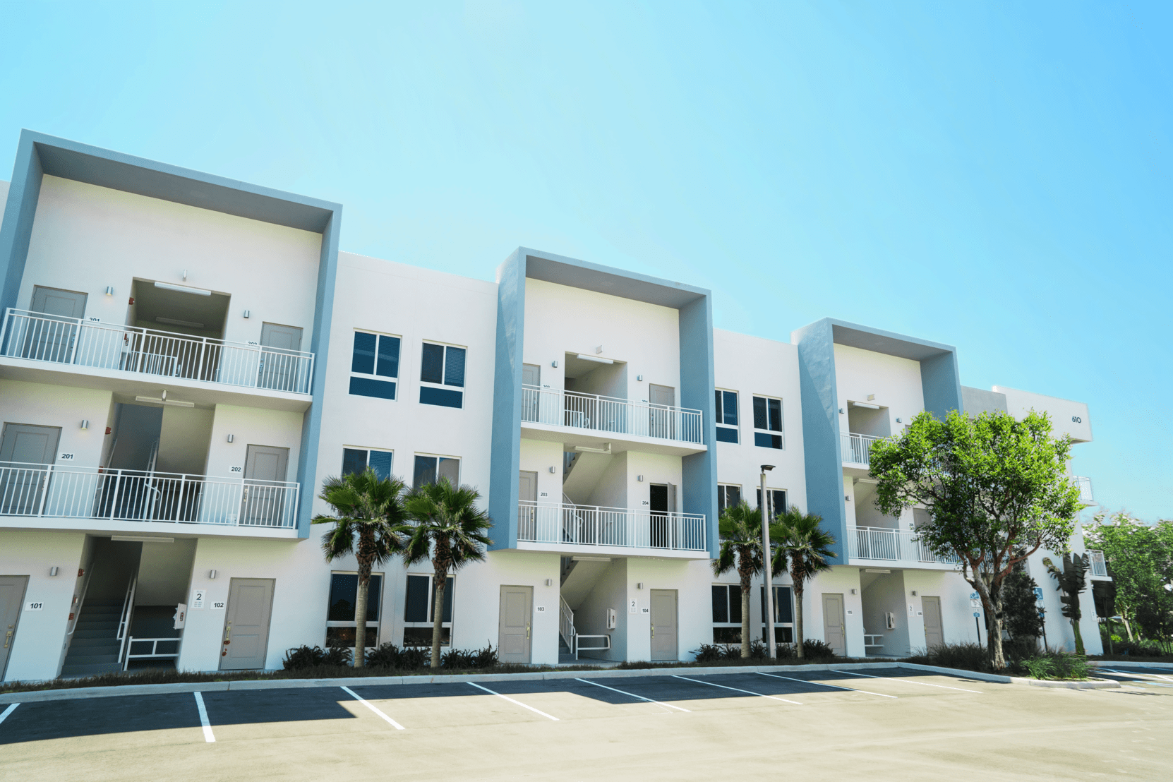 A large white apartment building with a parking lot in front of it.