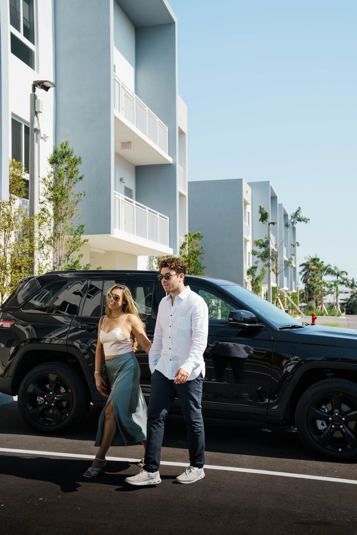 A man and a woman are walking down the street next to a car.