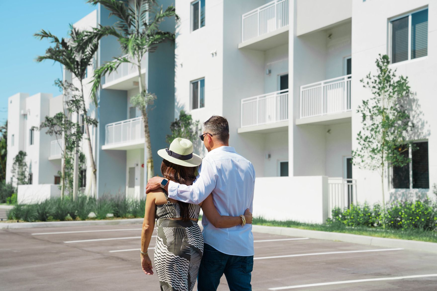 A man and a woman are walking in front of a white apartment building.