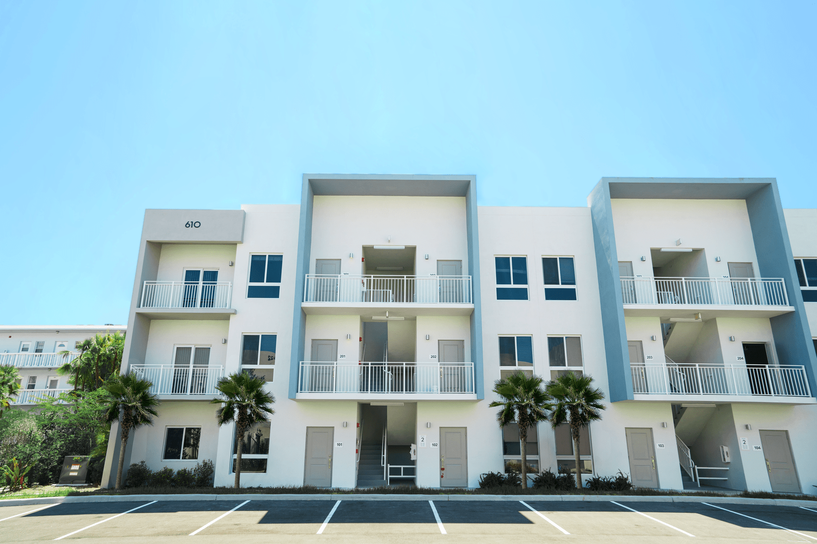 A white apartment building with balconies and palm trees in front of it