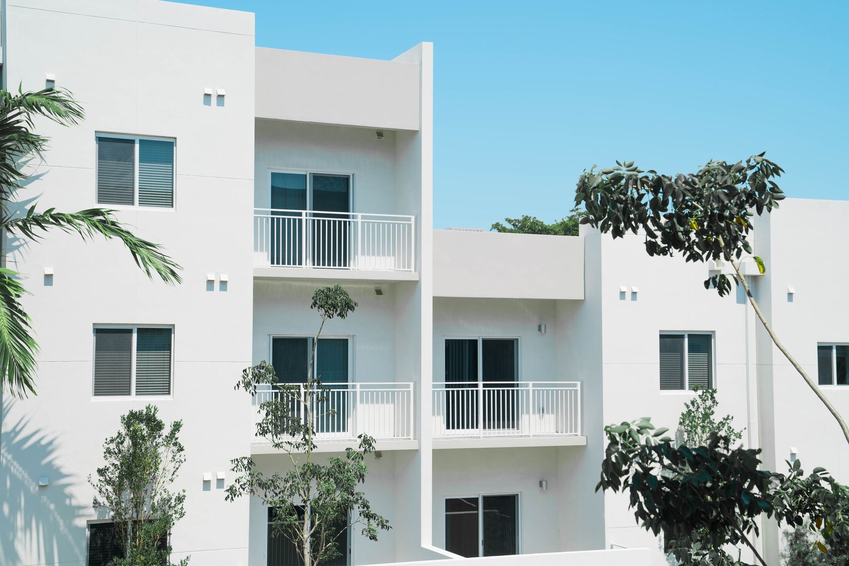 A white apartment building with balconies and trees in front of it