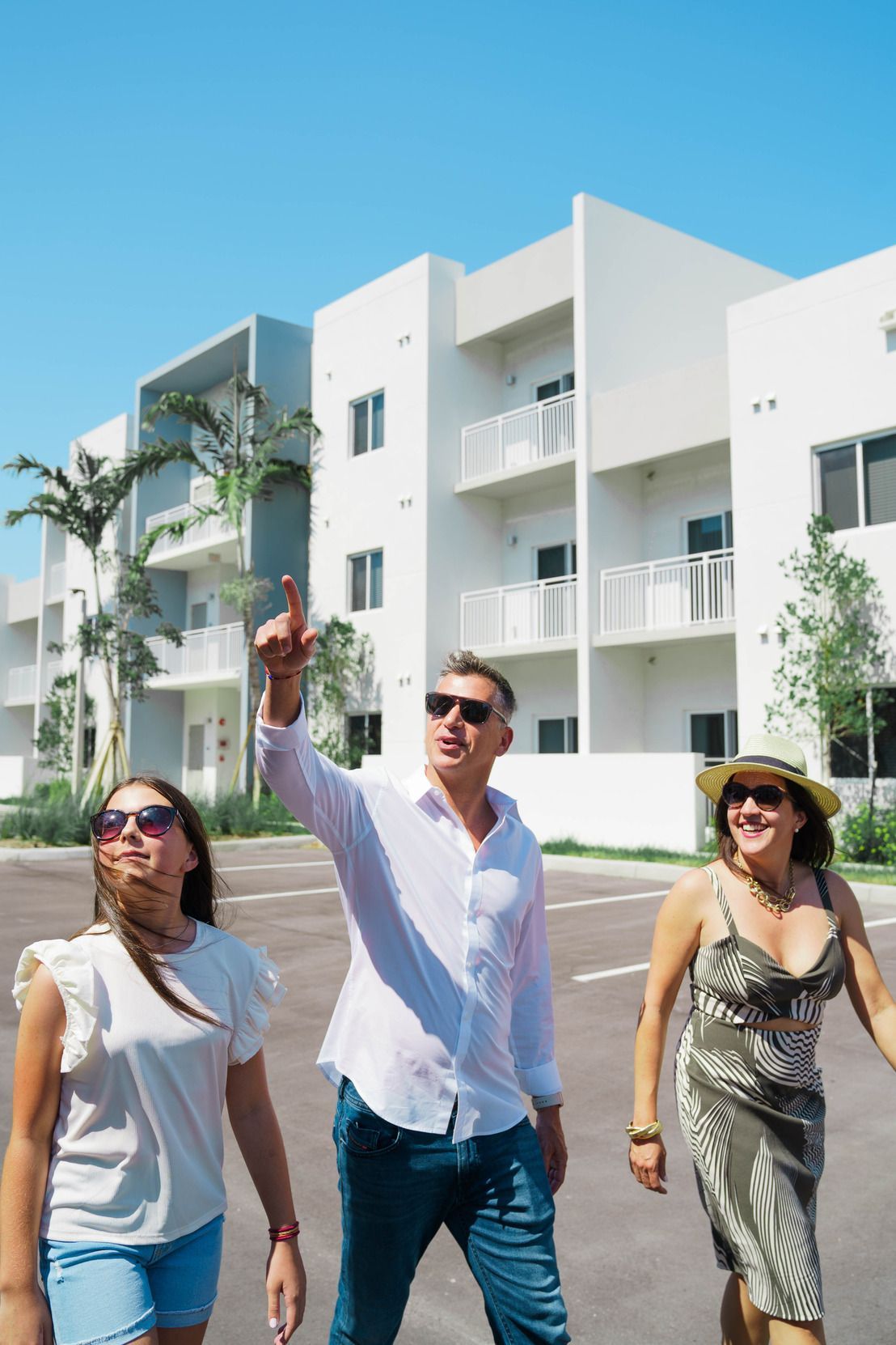A man and two women are walking in front of a white building.