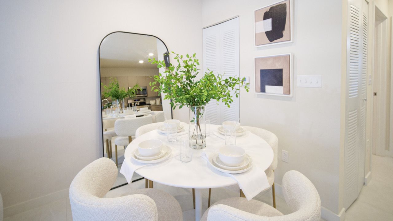 A dining room with a round table and chairs and a large mirror.
