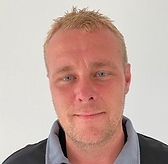 En mand med skæg og sort skjorte smiler til kameraet.