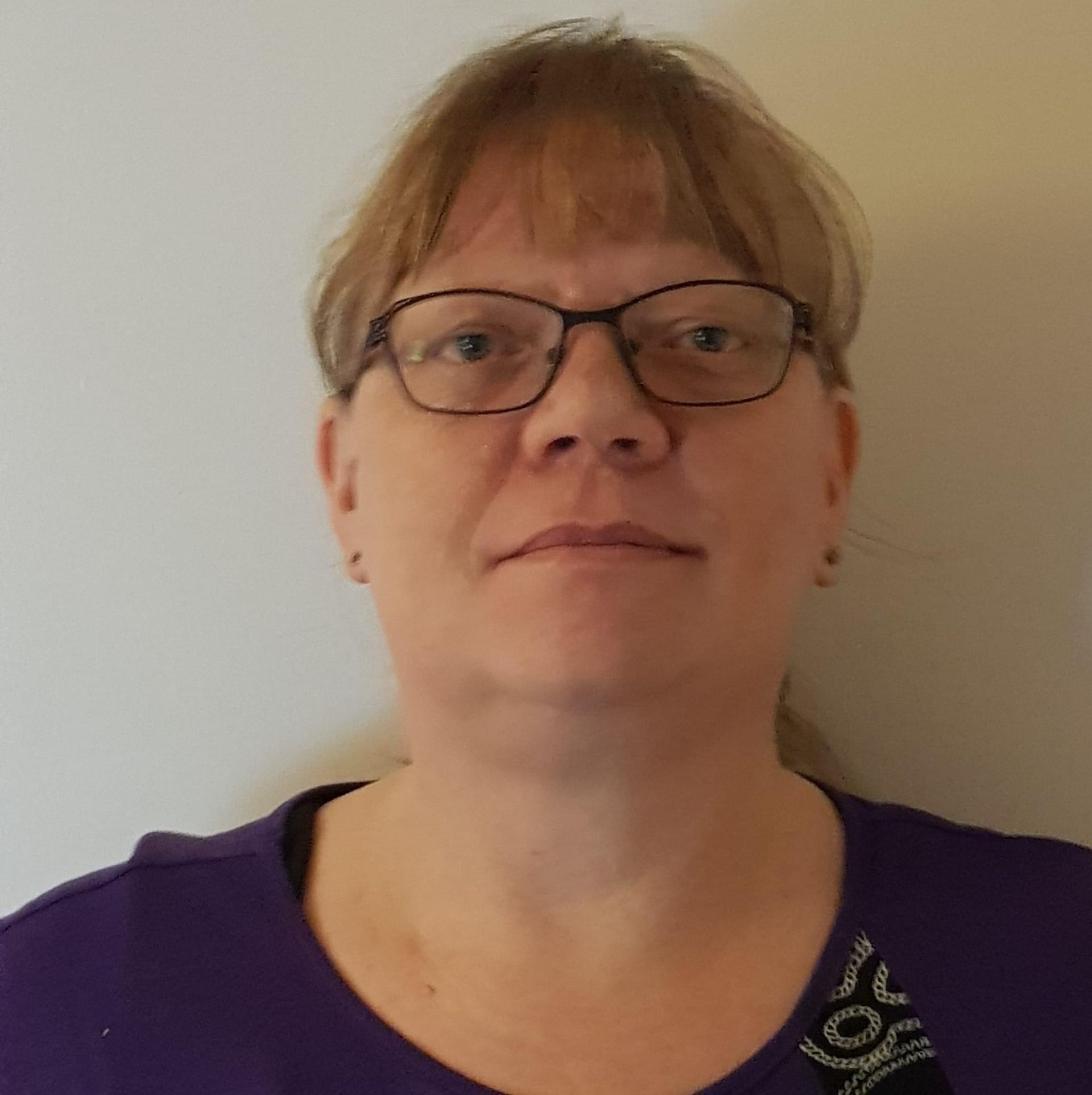 En kvinde iført briller og en lilla skjorte ser på kameraet.