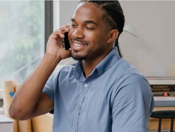 Um homem está sentado em uma mesa falando ao celular.
