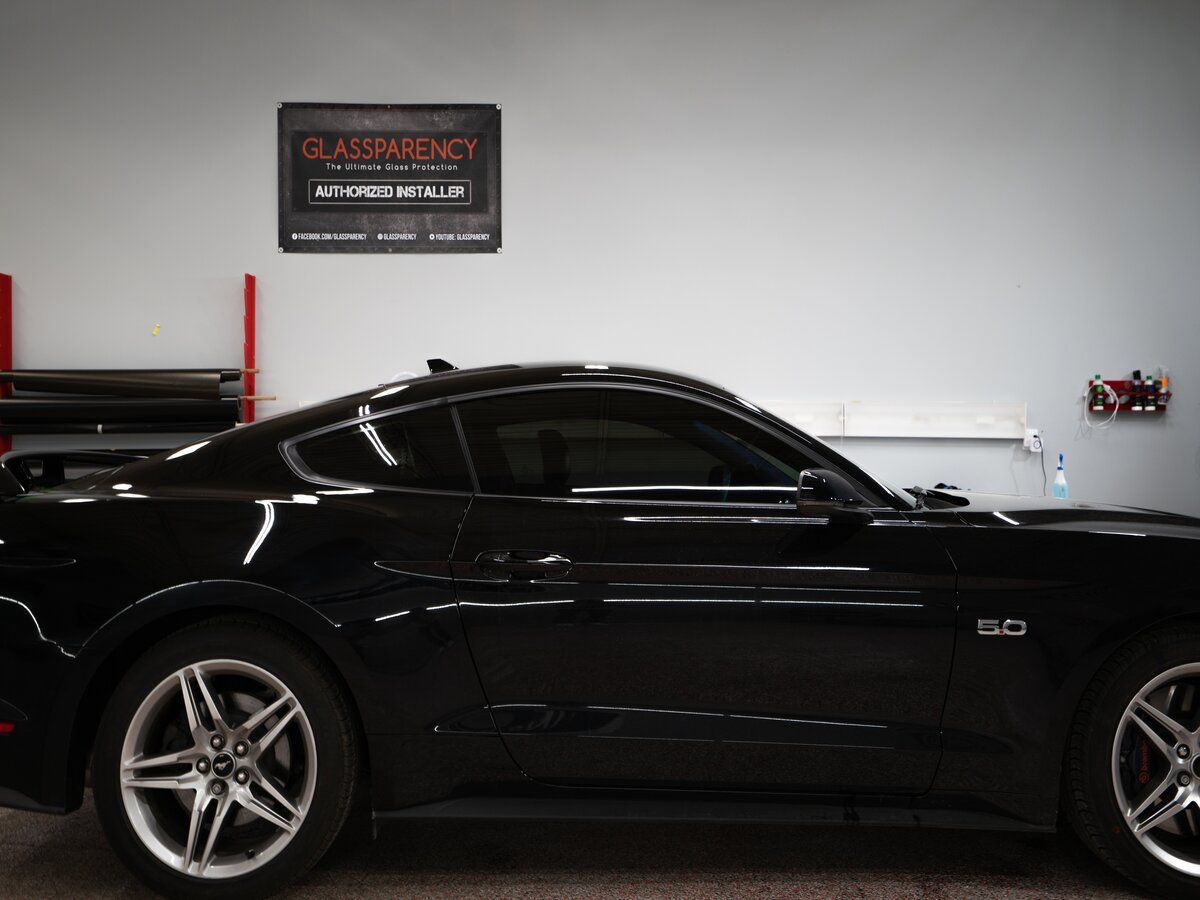 Black Mustang with tinted windows inside a garage. A business sign is on the wall.