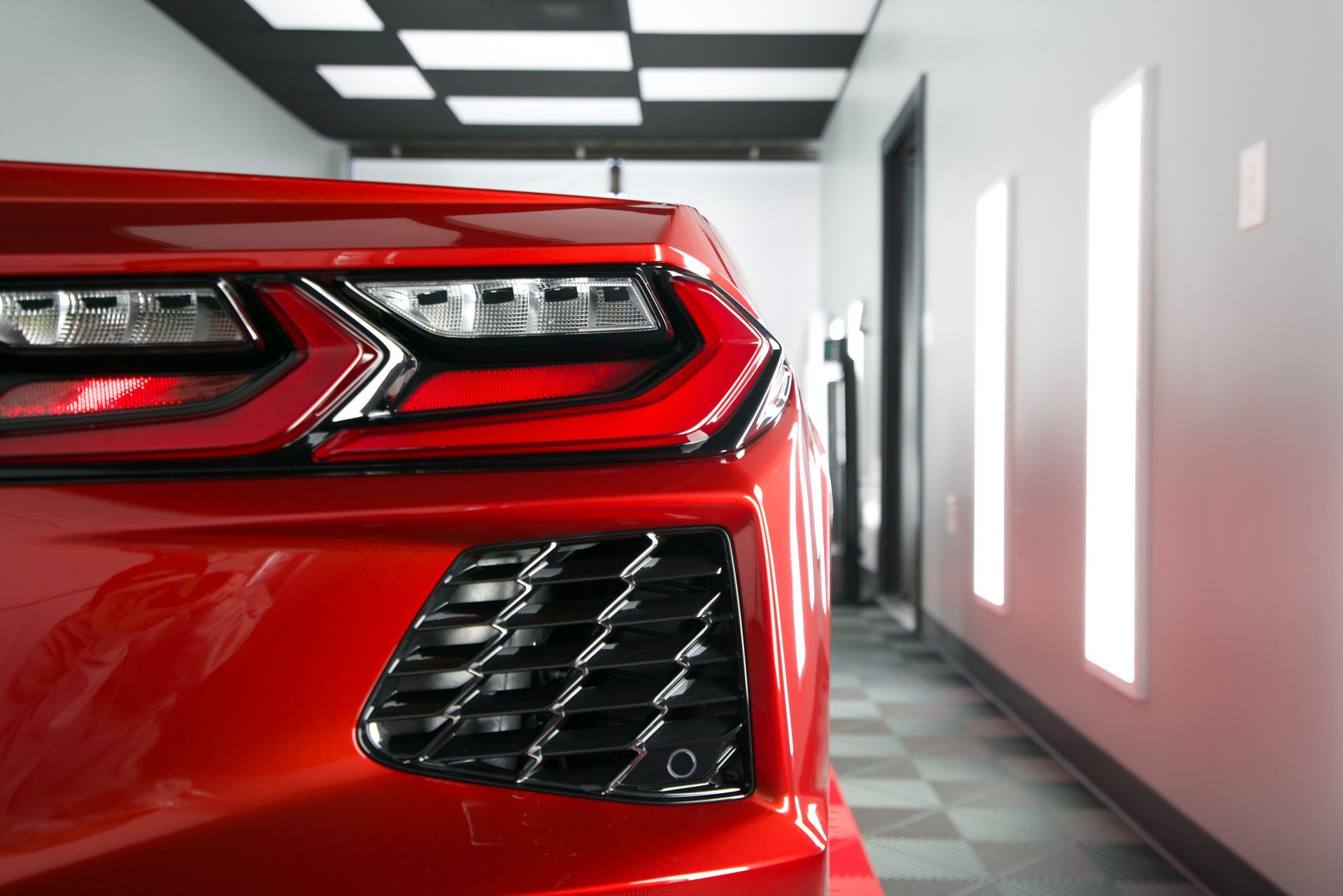 Red sports car's rear, with bright taillights, parked in a garage with checkered floor.