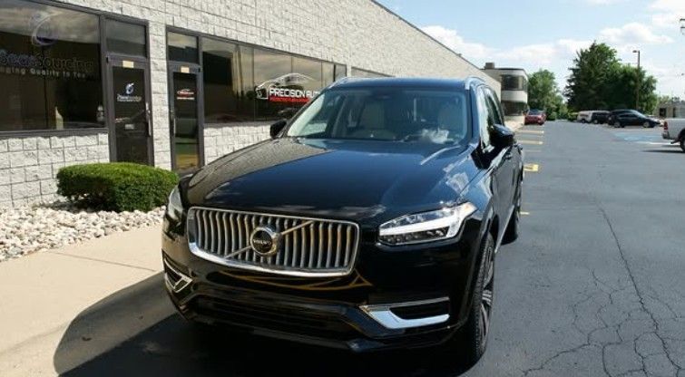 Black Volvo SUV parked in front of a building with glass windows, sunny day.