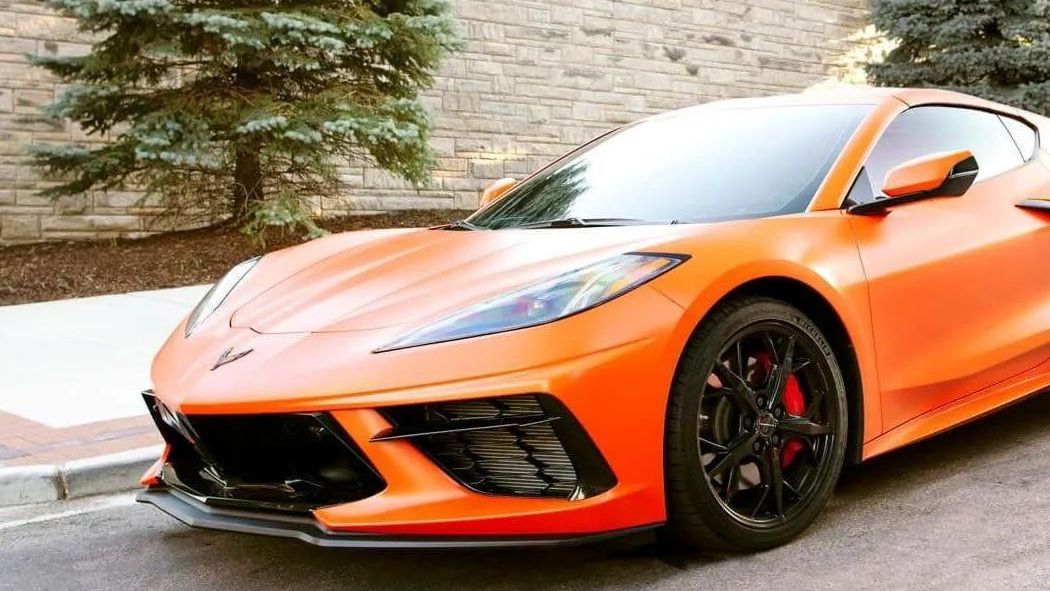 An orange corvette is parked on the side of the road.