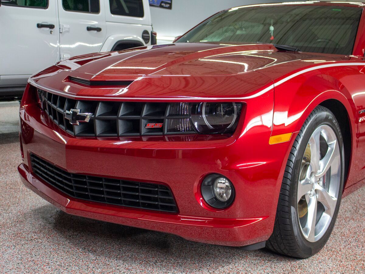 Red Chevrolet Camaro with black grille and headlights, parked indoors.