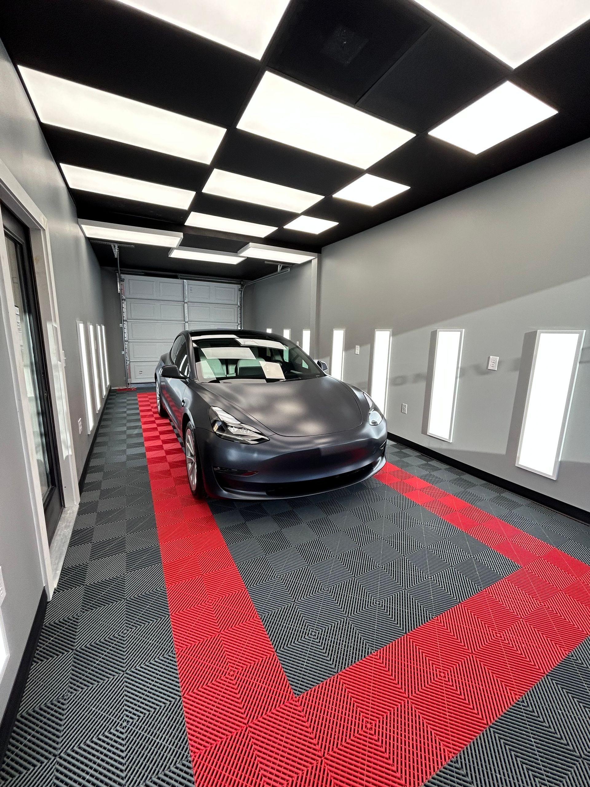 Tesla car in a detailing bay with red and gray flooring, white lighting, and a checkered ceiling.