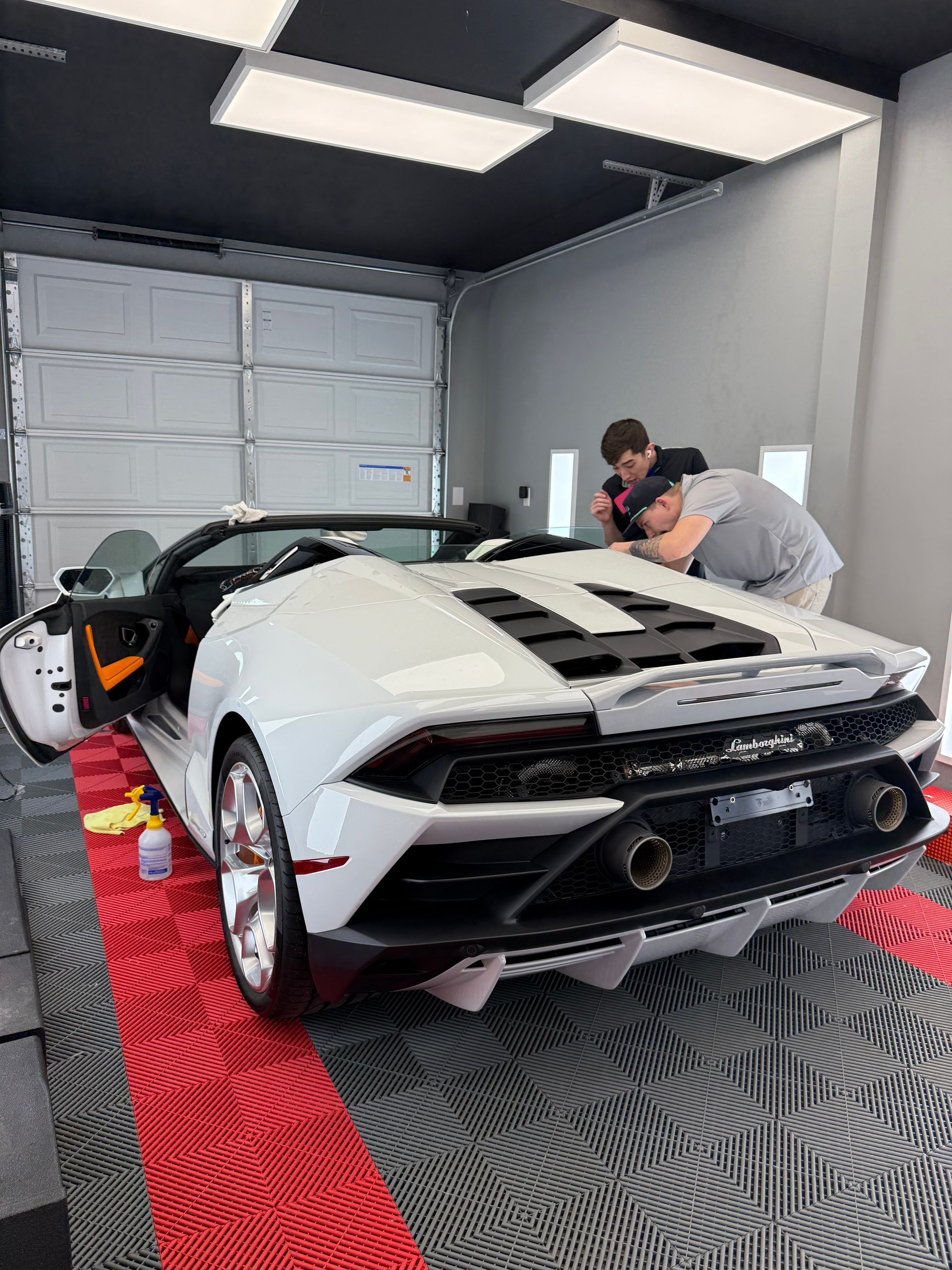 White Lamborghini convertible in a garage, two people working on the car.