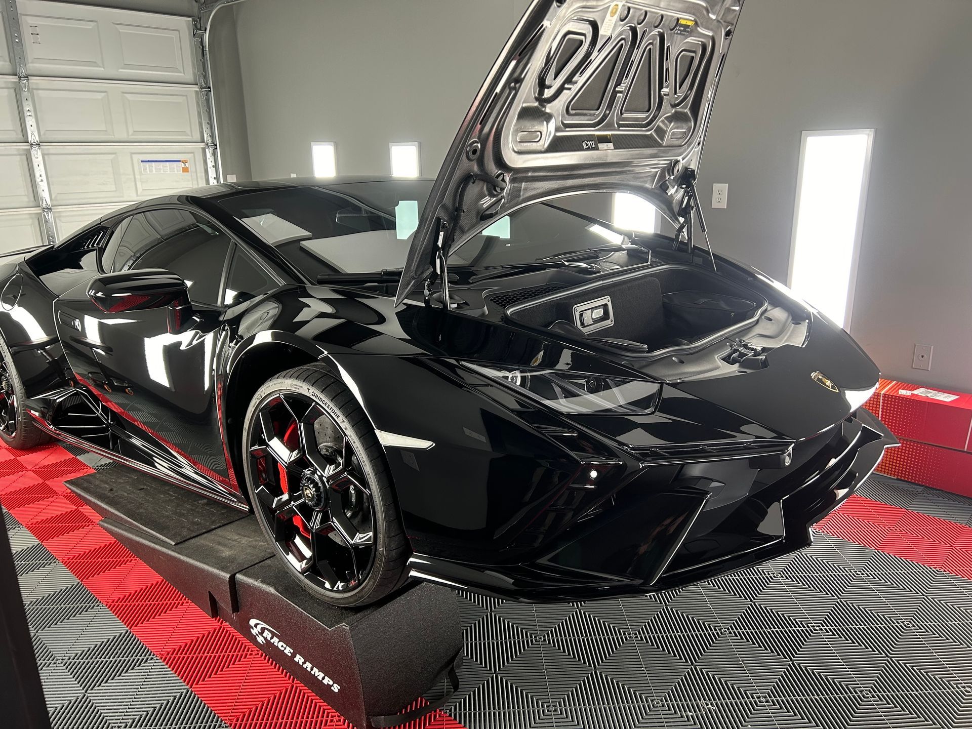 Black Lamborghini with hood open on a ramp in a garage.