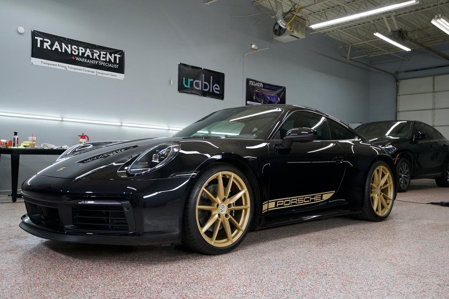 Black Porsche with gold wheels in a shop. 