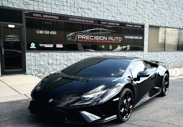 A black Lamborghini parked in front of a building with signs for Precision Auto featuring automotive services.