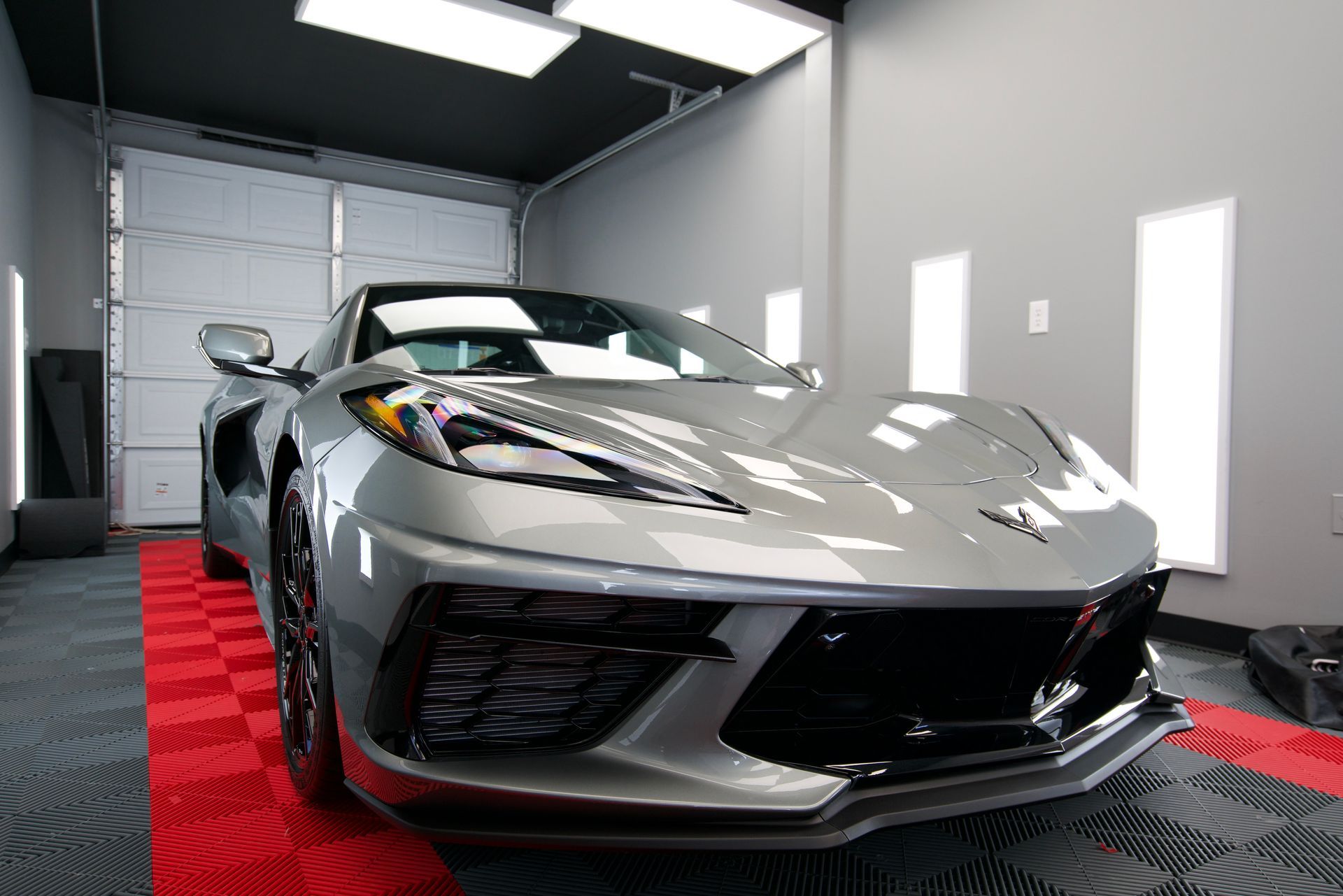 A silver corvette is parked in a garage next to a garage door.