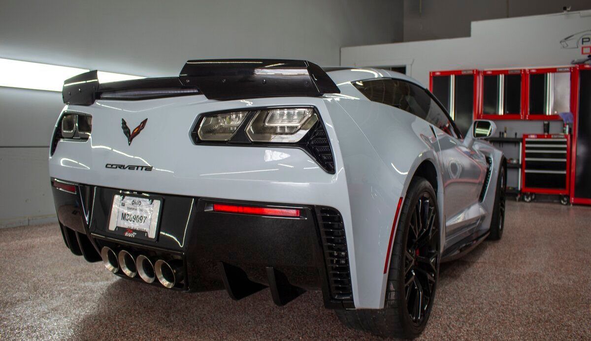 Rear view of a light gray Corvette with black accents in a garage.