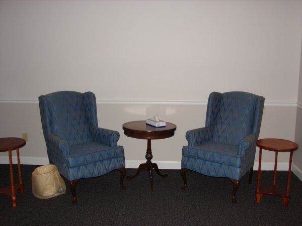 Two blue armchairs face each other, with a small round table between them. Another table is to each side.